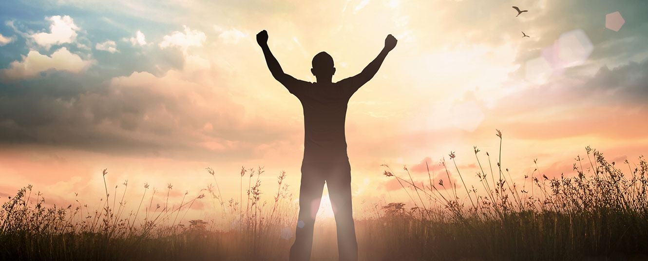 Man in field with arms raised to sky.