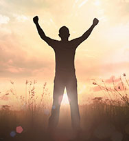 Man in field with arms raised to sky.