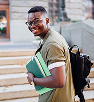 Student on campus holding books and backpack smiling.
