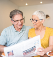Older couple wearing glasses reading newspaper at kitchen table